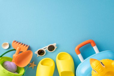 Mavi arka planda sıralanmış sandaletler, güneş gözlükleri, çanta ve oyuncaklar da dahil olmak üzere renkli yaz aksesuarları