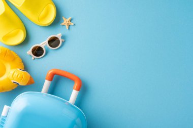 Sarı sandalet, güneş gözlüğü, şişme ördek ve mavi arka planda bavul.