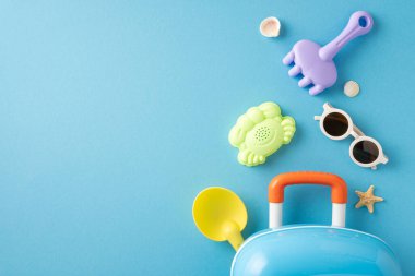 Parlak plaj oyuncakları, güneş gözlükleri ve mavi bir arka planda seyahat valizi.