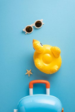 Mavi arka planda yaz temalı esasların en üst dikey görüntüsü, bavul, güneş gözlüğü, şişme ördek ve deniz yıldızı, seyahat kavramları, yaz tatilleri ve rahatlama titreşimleri için ideal.