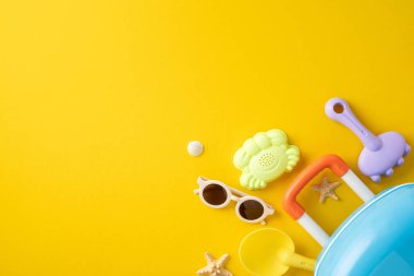 Renkli plaj oyuncakları ve seyahat gereksinimleri yaz eğlencesi için canlı sarı bir arka plana yerleştirildi. Güneş gözlüğü ve plaj kürekleri gibi çocuk eşyalarıyla tatil kavramlarını betimler.