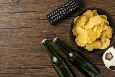 Bira şişeleri, bir kase patates cipsi, uzaktan kumanda ve futbol topu, evde atıştırmalık ve içeceklerle oynanan bir futbol maçı için mükemmel.