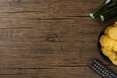 Patates cipsi, içecek şişesi ve ahşap bir yüzeye uzaktan kumanda.