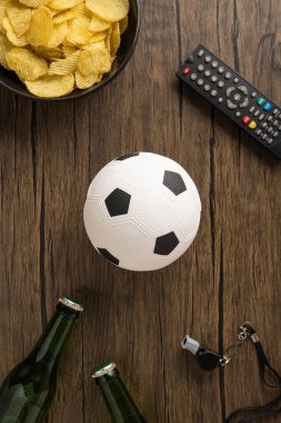 Evde maç izlerken futbol topu, cips, bira şişesi, uzaktan kumanda ve ıslık çalan rahat bir dümen.