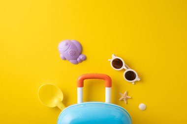 Canlı sarı arka planda plaj oyuncakları, güneş gözlükleri, küçük bir bavul ve yaz eşyaları yer alıyor.