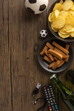 Patates cipsi, abur cubur, bira şişesi ve futbol detayları dikey ahşap bir masada.
