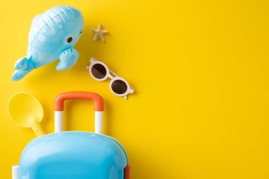 Bavul, güneş gözlüğü ve oyuncak balina da dahil olmak üzere renkli plaj eşyaları.