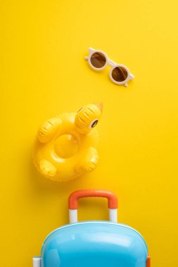 Güneş gözlüklü parlak dikey sarı zemin, şişme ördek ve renkli bir bavul, seyahat veya yaz temalı projeler için mükemmel.