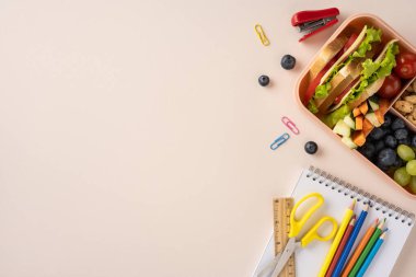 Renkli okul malzemelerinin yanında sandviç ve meyve içeren bir beslenme çantası.