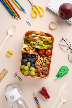 Okul malzemeleriyle çevrili taze meyve, fındık ve sandviçle dolu dikey bir beslenme çantası sağlıklı beslenme ve eğitici titreşimleri çağrıştırıyor..