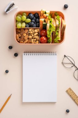 Sağlıklı atıştırmalıklar ve masanın üzerine bir defter ile yerleştirilmiş meyveler içeren dikey bir beslenme çantası.