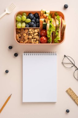 Bir not defterinin yanında meyve, sebze, fıstık ve sandviçlerle dolu dikey dengeli bir beslenme çantası..