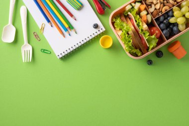 Okulun beslenme çantasının, renkli kalemlerin ve dokulu yeşil kağıtların yer aldığı yaratıcı bir kompozisyon.