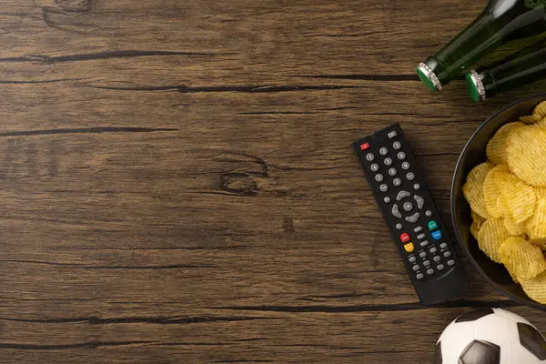 Kırsal bir masada uzaktan kumandalı, cipsli ve bira şişeli futbol sahnesi.
