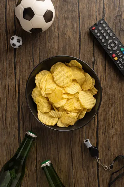 Dikey patates cipsi, futbol topları, bira şişeleri ve oyun gecesi gerekliliklerini gösteren tahta yüzey kumandası.