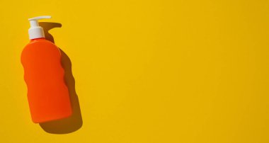 Canlı sarı arka planda pompası olan turuncu pankart plastik sıvı dağıtıcısı. Hijyen, ambalaj, kozmetik, minimalizm veya kişisel bakım konuları için ideal