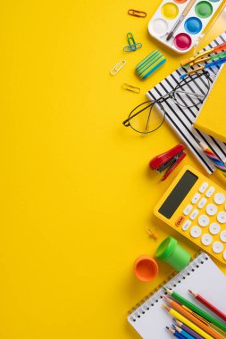 Kalemler, kalemler, hesap makineleri ve sarı arka planda boya gibi okul malzemelerinden oluşan dikey bir düzenleme. Eğitim, öğrenme ya da okul kavramları için mükemmel.
