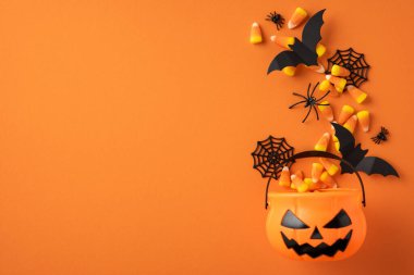 Mısır şekeri ve yarasalar ve örümcekler gibi Cadılar Bayramı öğeleriyle dolu turuncu balkabağı kovası.