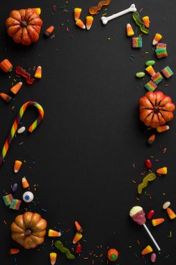 Renkli dikey Cadılar Bayramı şekeri, dekorasyonlar ve karanlık bir yüzey üzerinde sınır oluşturan mini balkabakları.