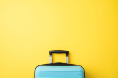 Zarif bir açık mavi bavul, yoğun sarı renkli bir duvar yüzeyinin önünde sergileniyor.