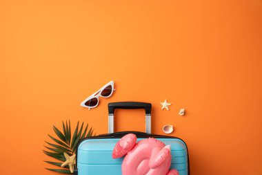 Güneş gözlüğü, deniz kabukları ve yaz tatilini temsil eden pembe flamingo ile tamamlanmış açık mavi bir bavul.