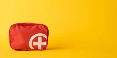 Kırmızı bir ilk yardım çantası parlak sarı bir arka plana yerleştirilir, hazırlık ve sağlık güvenliği vurgulanır. Görüntü acil durum çözümlerini, hazırlığı ve temel hayat kurtarma araçlarını sembolize eder..