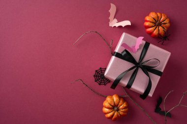 Siyah kurdeleli pembe hediye kutusu, sahte balkabakları, yarasalar ve örümcek ağlarıyla çevrili.