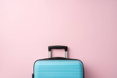 Minimalist kompozisyonda açık mavi bir bavul, yumuşak pembe bir arka planda, seyahat titreşimleri uyandırıyor.