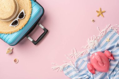 Yaz tatili hazırlıklarına ilham vermek için pembe arka planda bir bavul, hasır şapka, havlu ve plaj aksesuarları da dahil olmak üzere düz seyahat gereksinimleri