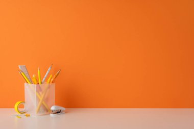 Beyaz masadaki sarı kırtasiye malzemelerini turuncu arkaplana karşı içeren basit çalışma alanı