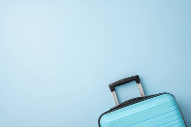 Pastel mavi arka planda siyah saplı açık mavi bir bavul seyahat ve tatilleri çağrıştırıyor.