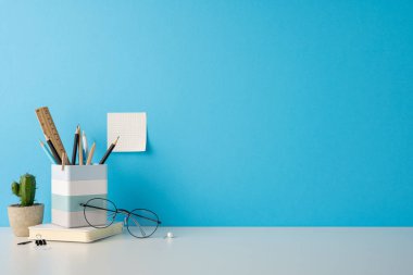 Masa düzenleme gözlük, kalem ve not defterleri sağlam mavi bir arka plana karşı