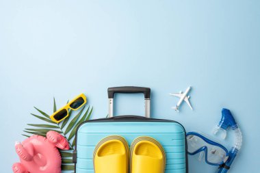 Bavul, aksesuarlar ve tropikal dekor da dahil olmak üzere seyahat ve tatil esaslarının düz kompozisyonu, tropikal ve sakin bir temayı çağrıştırıyor.