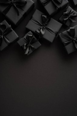 Siyah kağıda sarılı hediye kutuları dikey koyu bir arka planda fiyonklu modern ve sofistike bir stil yaratıyor.