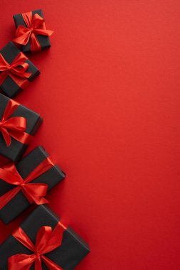 Kırmızı yüzey üzerine kırmızı kurdelelerle bağlanmış siyah hediye kutularının stilize edilmiş dikey dizilişi