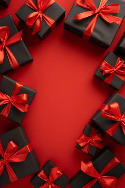 Kırmızı kurdeleye sarılı siyah dikey hediye kutuları zarafeti sembolize eden kırmızı bir yüzeye yerleştirilmiş.