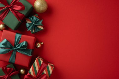 Dekoratif Noel temalı hediyeler fiyonklarla süslenmiş, kırmızı bir fonda şenlikli süslerle eşleştirilmiş.