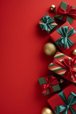 Dikey kırmızı bir yüzey üzerinde zarif fiyonklarla süslenmiş güzel paketlenmiş Noel hediyeleri dizisi