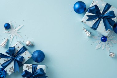 Zarif bir tatil düzeni. Mavi tonlarda hediye kutuları, süsler ve hafif arka planda mevsimlik dekorasyonlar var.