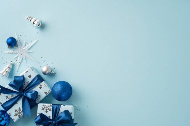 Mavi ve gümüş süslemeleri, yaylarla paketlenmiş hediyeler ve neşeli bir tatil atmosferi yaratan hafif bir arkaplanda süslerin yer aldığı şenlikli bir Noel düzenlemesi