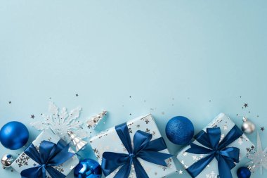 Mavi temalı dekorasyonlar, şenlikli kurdeleler ve açık arkaplanda süslerle süslenmiş zarif bir Noel hediyesi.