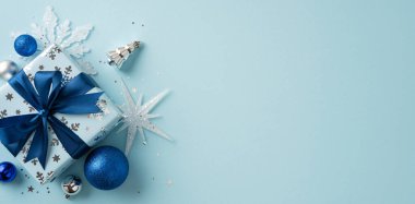 Bayram süslemeleriyle çevrili, mavi fiyonklu bayram kağıdına sarılı zarif bir Noel hediyesi.