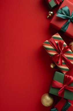 Şık dikey Noel hediyeleri, canlı kırmızı bir yüzeye takılmış kurdele ve süslemeler.