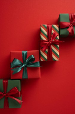Renkli paketlenmiş tatil hediyeleri ve dikey kırmızı arka planda dizilmiş kurdeleler.