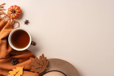 Sıcak ve cezbedici sonbahar temalı bir daire, bir fincan çay, rahat turuncu eşarp, küçük balkabağı ve tarafsız bir arkaplanda dekoratif yaprak kesikleri yer alıyor.