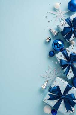 Güzel paketlenmiş Noel hediyelerinin yanında mavi kurdeleler ve şenlik süsleri. Mavi arka plandaki zarif dikey kompozisyon mevsimsel neşe taşır