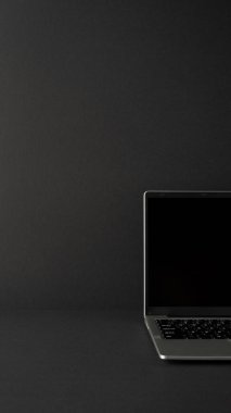 Pürüzsüz koyu renkli bir yüzeye yerleştirilmiş, profesyonel ve modern çalışma alanındaki verimliliği ve teknolojiyi simgeleyen, minimalist tasarımı olan, açık, dikey bir dizüstü bilgisayarın resmi