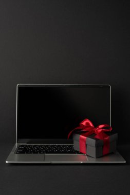 Bir dizüstü bilgisayar ve kırmızı kurdeleli bir hediye kutusu içeren zarif çalışma alanı dikey kurulumu modernlik, iş memnuniyeti ve profesyonel bir ortamda şenlik temalarını yansıtıyor.