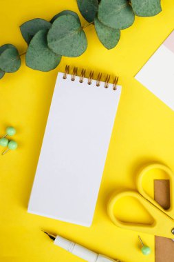 School supplies concept. Photo of white and yellow stationery, pen, scissors and paper notebook on a yellow background