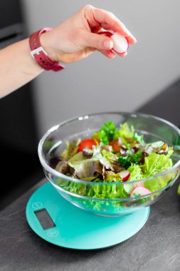 A girl preparing a healthy salad using kitchen scale